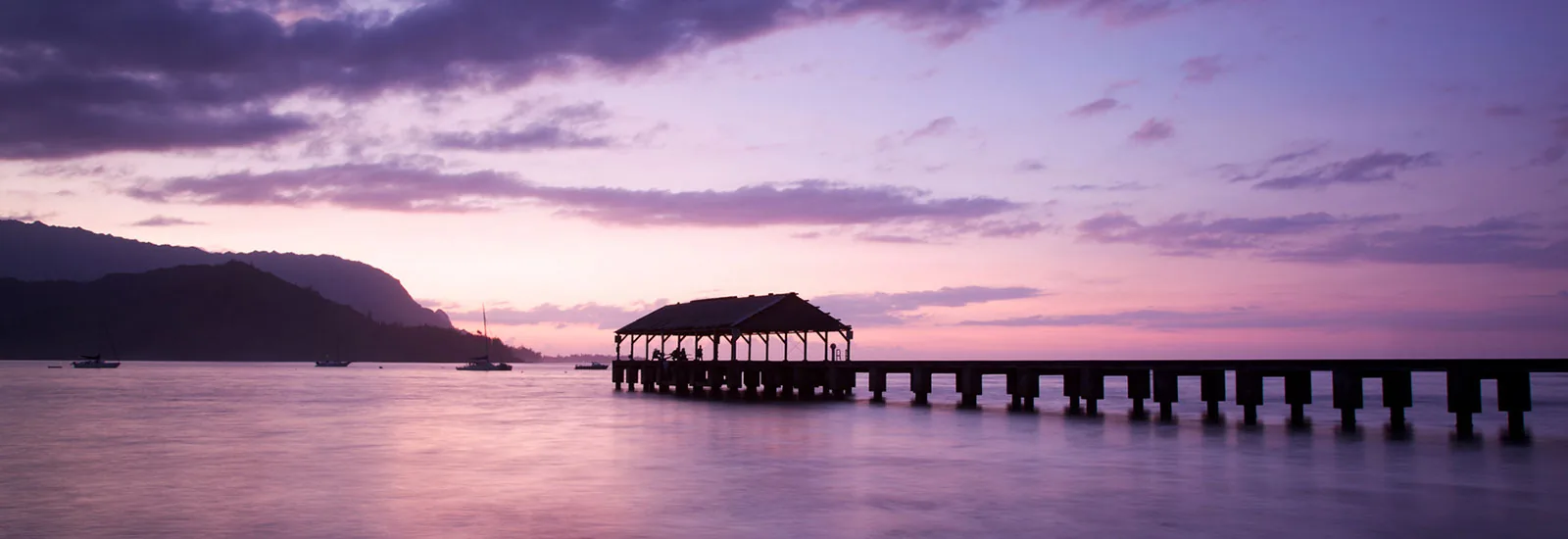 Hanalei Pier reaching into a calm bay under a soft twilight sky on Kauai's north shore